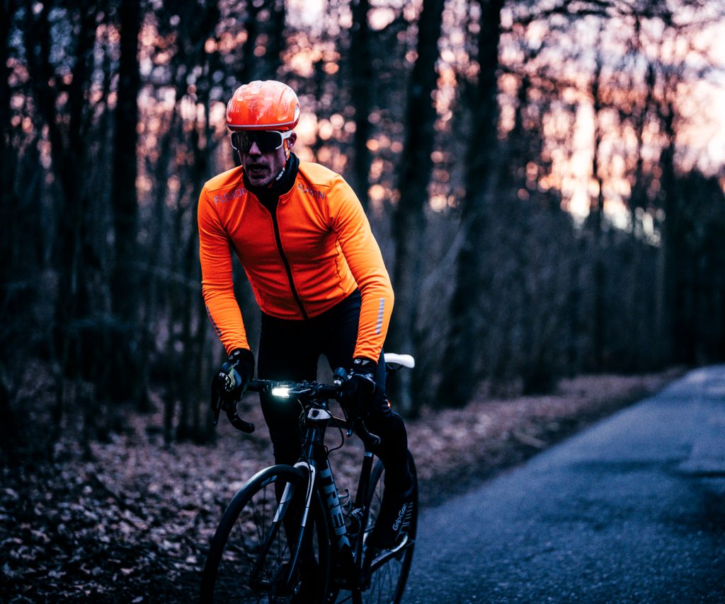 Cyclist in an orange FUSION jacket on a forest road at dusk