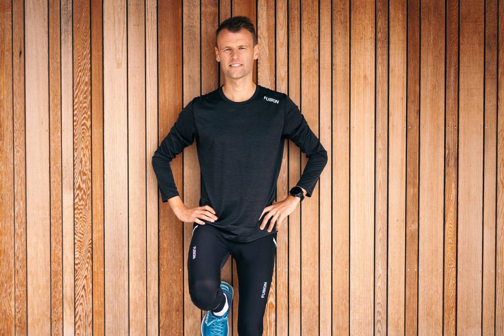 Man in a black FUSION top against a wooden wall